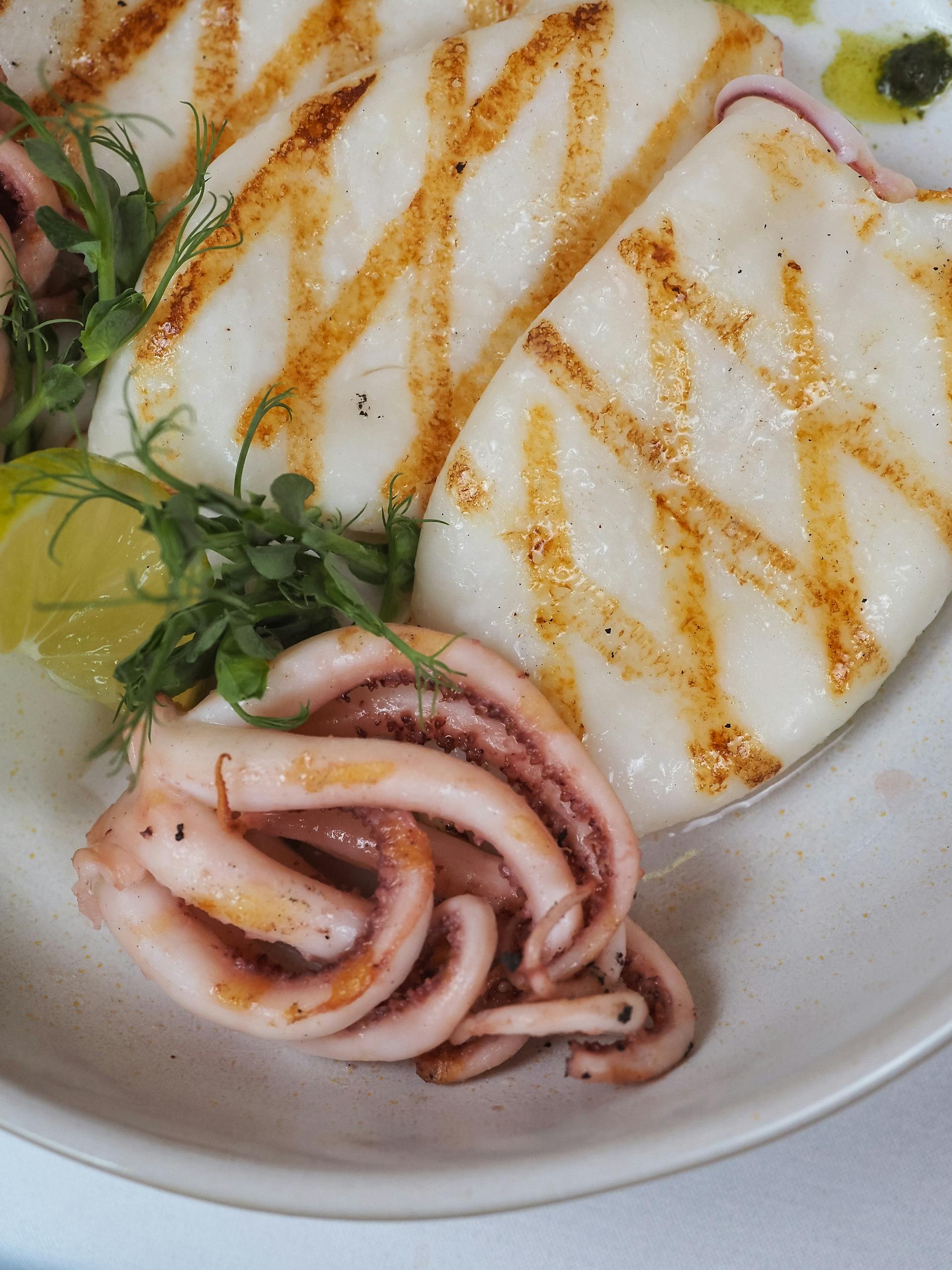 Delicious grilled squid served with lemon and greens on a white plate.